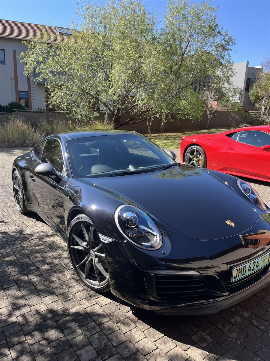Freshly detailed black Porsche 911 Carrera on a driveway, with a red Ferrari 458 behind it